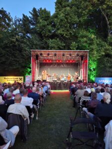 Bühne im Schlosspark Bisamberg mit Sängerin und Musikerinnen und Musikern, davor sitzendes Publikum
